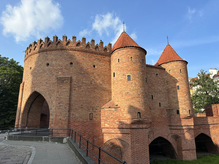 Brick castle features unique towers and crenellated walls, set against a backdrop of lush greenery and clear blue sky, representing historical significance and architectural beautyの写真素材