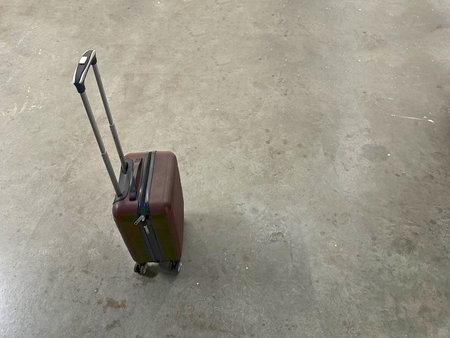 Dark suitcase with a retractable handle rests on a polished concrete floor, emphasizing modern travel aesthetics and functionality in a minimalist environmentの写真素材