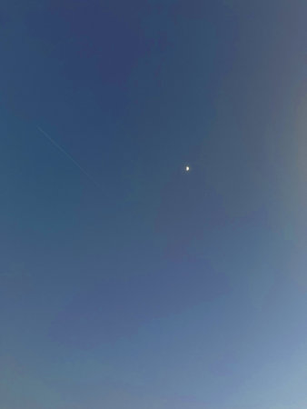 Expansive blue sky features a luminous moon and a subtle airplane trail, evoking a peaceful...