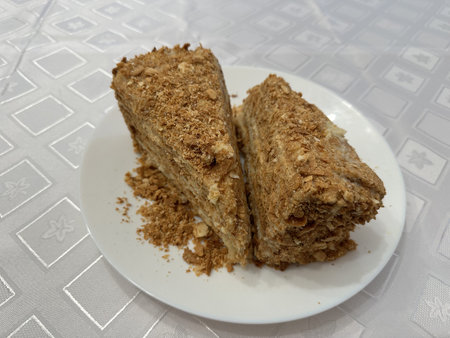 Two pieces of honey cake with a crumb topping are displayed on a white plate, set against a...