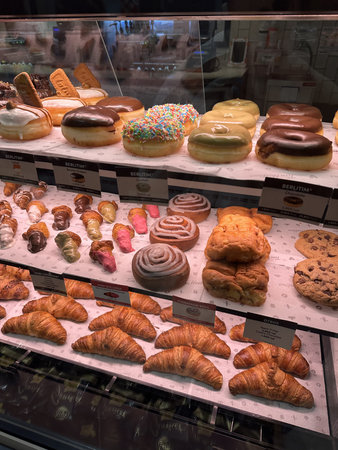 Display case filled with a variety of pastries and donuts, showcasing colorful icing, sprinkles, and...
