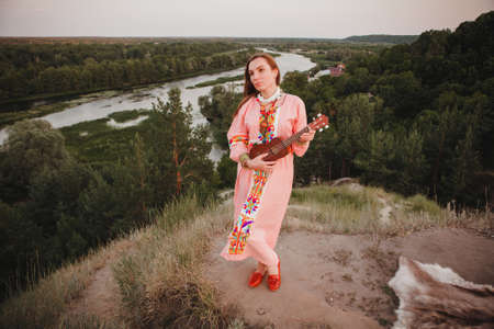 portrait young woman in ethnic dress lies with ukulele in handsの写真素材
