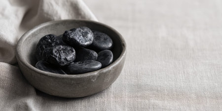 A bowl filled with smooth black stones rests on a neutral fabric surface. The arrangement creates a calm and minimalist atmosphere, perfect for decor or meditation.の素材