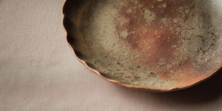 A rustic, handmade plate rests on a smooth, neutral fabric. The plate displays unique textures and earthy colors, showcasing artisanal craftsmanship and natural beauty.の素材
