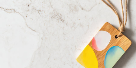 A wooden tag with bright colors rests on a smooth marble surface. Natural light highlights its shape and design, creating an inviting and vibrant atmosphere.の素材