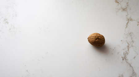 A single walnut rests on a smooth white marble countertop, illuminated by bright light, showcasing its unique texture and shape. The setting is simple and minimalistic.の素材