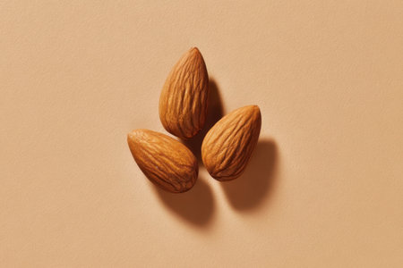 Three almonds are arranged on a smooth brown surface, showcasing their textured shells. The lighting creates soft shadows, highlighting their natural shapes and colors.の素材
