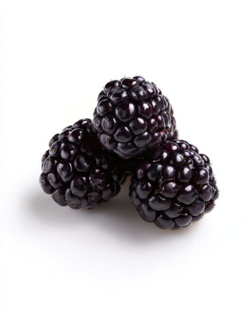 Three plump, ripe blackberries are arranged closely together on a bright white surface, showing their shiny, dark skin and unique texture.の素材