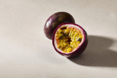 Bright purple passion fruit lies on a light surface, one half opened to reveal its vibrant yellow pulp filled with seeds, inviting a taste of tropical flavor.の素材