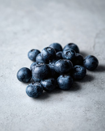 A cluster of fresh blueberries sits on a gray stone surface, showing their rich blue color and round shape, perfect for healthy snacking or cooking.の素材