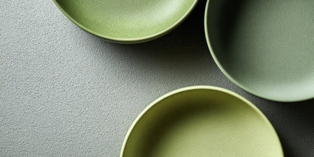 Three simple green plates are placed on a soft gray background, highlighting their smooth surfaces and minimalist design for a stylish dining experience.の素材