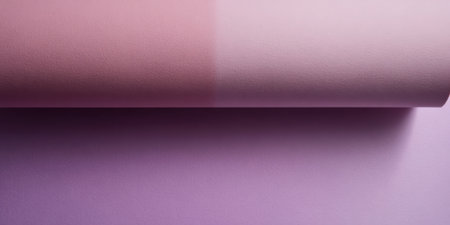 A close-up view of a rolled sheet of paper displaying a gradient from a soft pink to a light lavender. The paper is placed on a neutral-colored surface, suggesting a creative setup.の素材