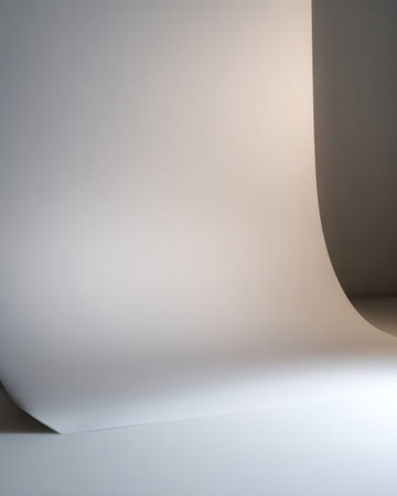 A large sheet of smooth white paper curves gracefully against a soft light in a studio setting. This backdrop offers a clean and elegant surface for creative projects.の素材