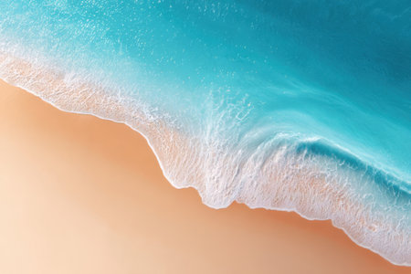 Ocean waves crash gently on the shore of a sandy beach. Clear blue water meets light-colored sand under the bright sun, creating a vibrant scene in the daytime.の素材