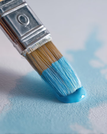 A brush with blue paint touches a white surface. The blue paint spreads as the bristles move. This moment captures the process of creating artwork with color.の素材