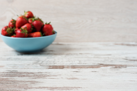 Blurred effect background. Pile of juicy ripe organic fresh strawberries in a large blue bowl. Light rustic wooden background.の写真素材