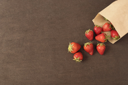 Paper bag with fresh red strawberries. Fresh strawberries in a small bag on a wooden style surface. Small group of strawberries on dark wood background with copy spaceの写真素材