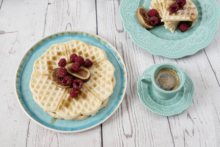 Soft Belgian heart shaped waffles with raspberries and figs, covered with honey on turquoise blue plate and coffee. Rustic wooden background, top view. Holiday morning at homeの写真素材