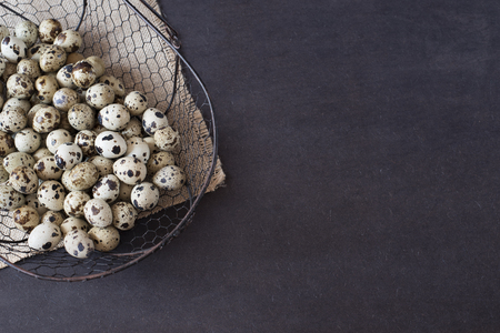 Wire mesh basket with quail eggs. Dark food photography. Rustic background, selective focus and diffused natural light. A different type of concept image for Easter. Copy space.の写真素材