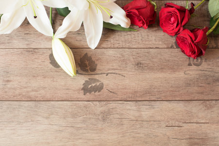 Floral frame with stunning white lilies and red roses on wooden background. Copy space. Wedding, gift card, valentine's day or mother's day backgroundの写真素材