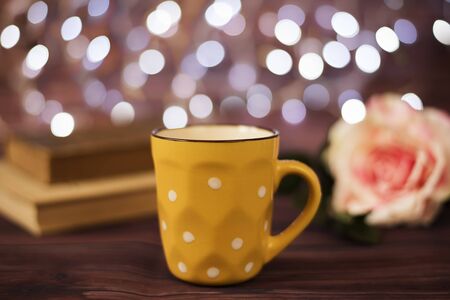 Coffee cup, tea, old books and rose on wood table in cafe with bokeh light background. Leisure lifestyle concept. Coffee on table in the night. Rustic background with beautiful Christmas lights of bokeh. Perfect winter time treat.の写真素材