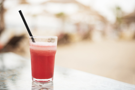 Red cocktail, watermelon fresh on a table, close up. On the background blurred umbrellas on the beach. Sun, haze, glareの写真素材