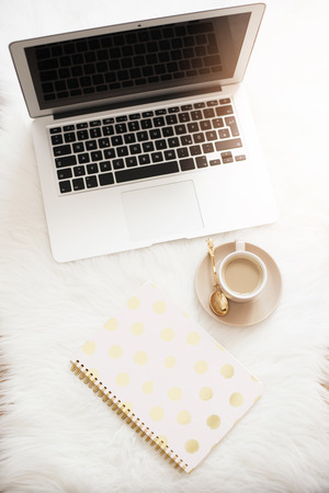 Laptop, coffee and notebook on the floor on a white fur carpet. Freelance fashion comfortable femininity home workspace in flat lay style. Top view, pink and gold. Vertical imageの写真素材