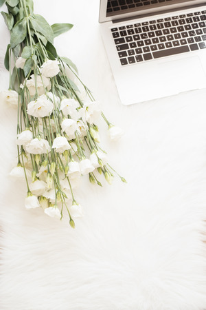 Laptop and a large bouquet white flowers on the floor on a white fur carpet. Freelance fashion comfortable femininity home workspace in flat lay style. Top view, pink and gold. Vertical imageの写真素材