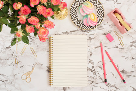 Feminine workplace concept. Freelance fashion comfortable femininity workspace in flat lay style with flowers, golden pineapple, notebook on white marble background. Top view, bright, pink and goldの写真素材