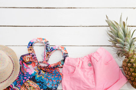 Straw Hat, Tropical Print Swimsuit, Pink Jeans Shorts, Pineapple. White Old Wooden Background