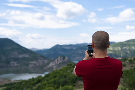 Young Man Taking Pictures With Mobile Smartphone Of Mountain and Landscape.の写真素材