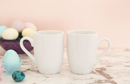 Two White Mugs Mockup - Easter theme. Easter eggs. Colorful eggs in matte colors. Light marble backgroundの写真素材