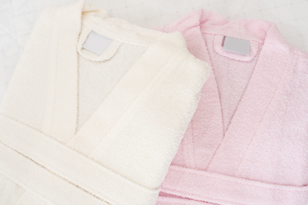 Folded bathrobe on bed in room. White and pink, two robesの写真素材