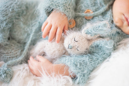 Newborn Baby. Sleeping Baby In Bed, Holding A Bunny Toy. Baby With Blue Knitted Romper