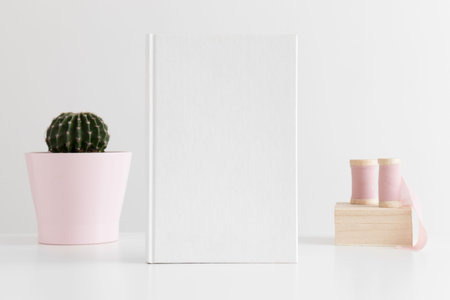 White book mockup with silk ribbons and a cactus in a pot on white table.