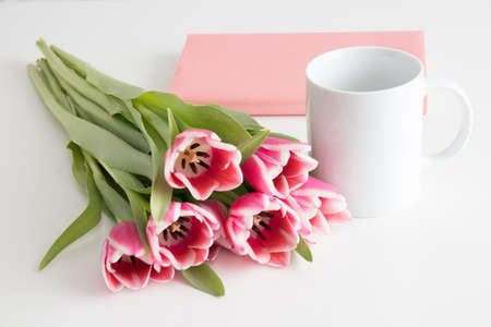 Bouquet of pink tulips, mug and book on a white table.の写真素材