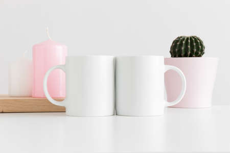 Two mugs mockup with candles and a cactus in a pot on white table.の写真素材