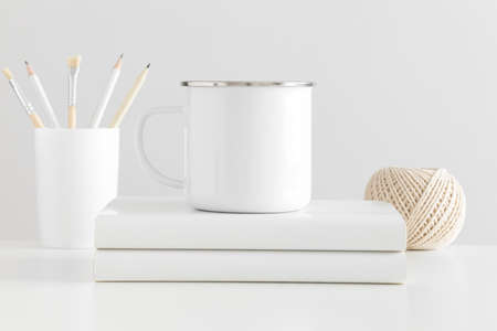 Enamel mug mockup with workspace accessories on a white table.の写真素材