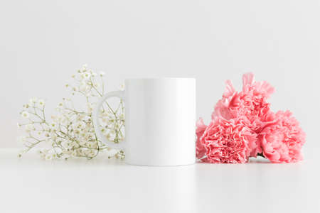 Mug mockup with a bouquet of pink carnations and a gypsophila on a white table.の写真素材