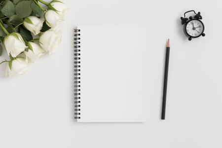 Top view of a notebook mockup with a bouquet of roses on a white table.