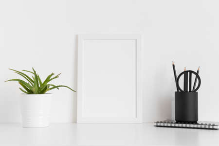 White frame mockup with a succulent plant and workspace accessories on a white table. Portrait orientation.の写真素材