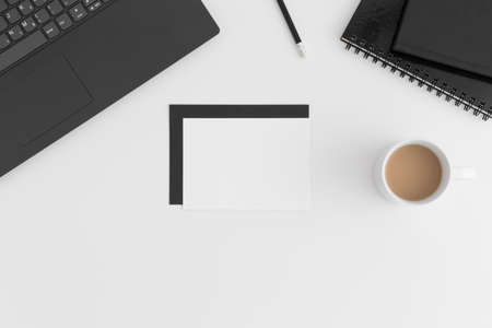 Top view of a white card mockup and envelope with a laptop, cup of coffee and workspace accessories on a white table.の写真素材