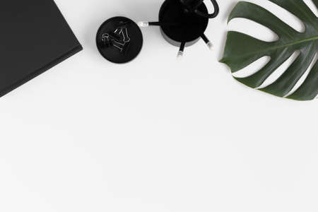 Workspace accessories and a monstera leaf on a white table.  Flat lay with blank copy space.の写真素材