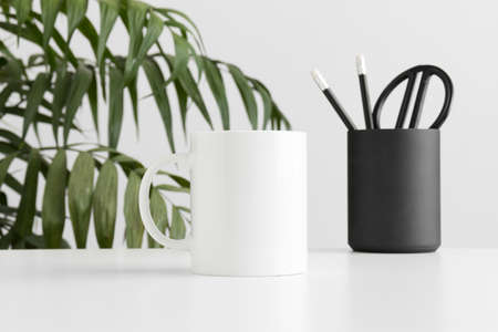 Mug mockup with workspace accessories on a white table and a palm plant.の写真素材