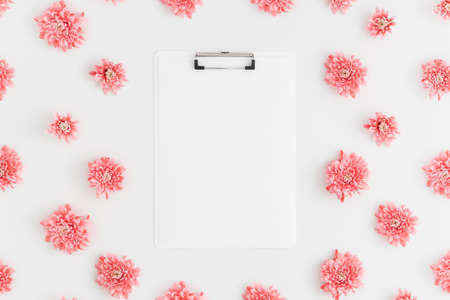 Top view of a white clipboard mockup with pink chrysanthemum decoration on a white background.の写真素材
