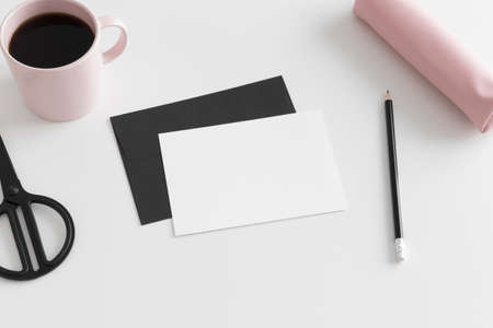 Top view of a white card mockup and envelope with workspace accessories and a cup of coffee on a white table.の写真素材