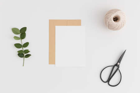 Top view of a white card mockup and envelope with twine, scissors and green branch on a white table.の写真素材