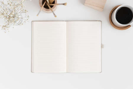 Top view of a notebook mockup with workspace accessories and a gypsophila in a vase on a white table.の写真素材