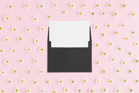 Top view of a white card mockup with daisy decoration on a pink background.