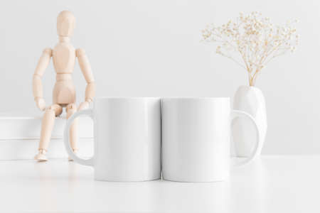Two white mugs mockup with books, manikin and a gypsophila in a vase on a white table.の写真素材